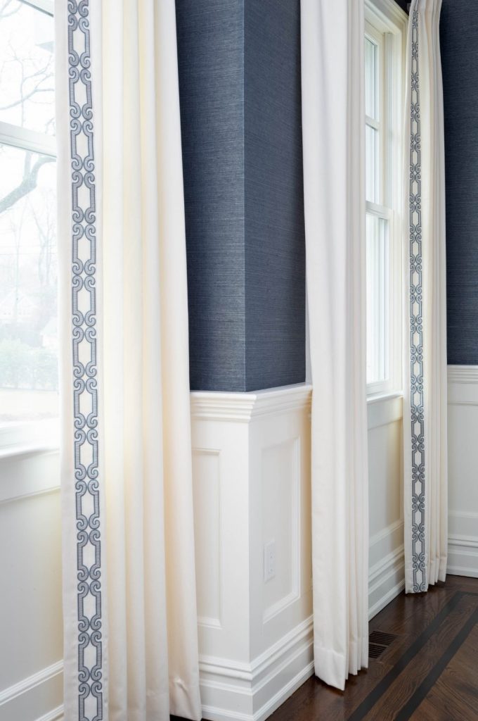 Dining room design, NJ Interior Designer. Blue grasscloth wallpaper with white drapes and blue trim detail, white paneling along bottom side of wall. 