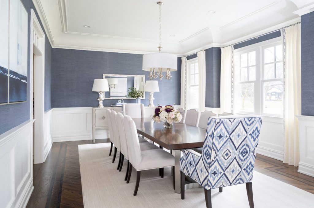 Dining room design, NJ Interior Designer.  Long wood rectangular dining table, blue grasscloth wallpaper, white drapes, low hung light fixture, white side chairs and a bold blue host chair. 