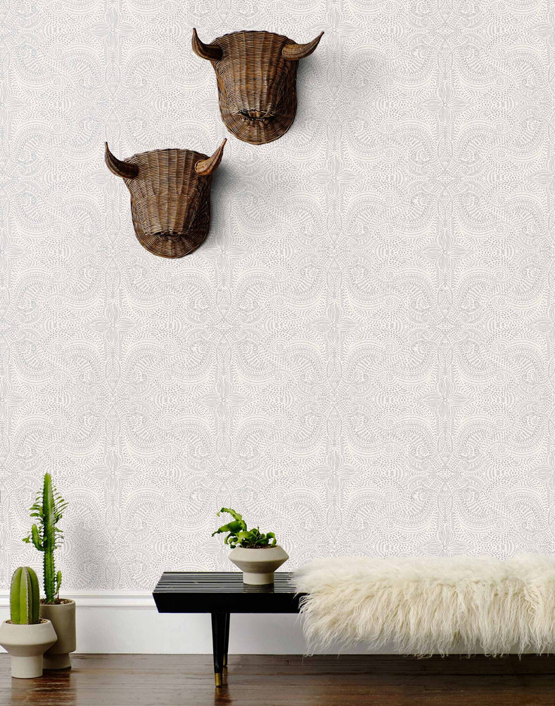 white and silver dainty printed wall paper with woven decor on wall, bench with furry blanket and cacti.