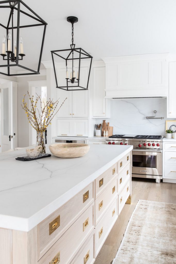 quartz kitchen counter top on island with bowls and flowers in a vase. Pendant lighting, white cabinets, light hardwood and runner. 