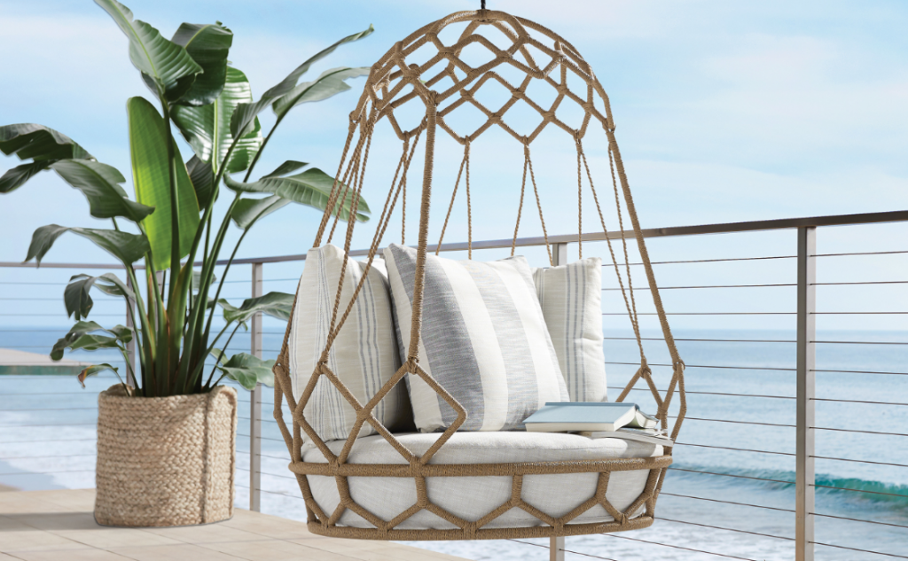hanging rattan and wicker chair with pillows and seat cushion, large faux plant and ocean view.