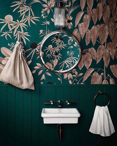 green bathroom with old sink, pink and green floral wallpaper and circular mirror. 