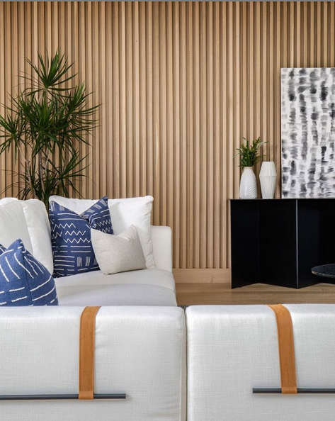 mid tone wall paneling interior design with plants, l shaped white couch with blue pillows. 