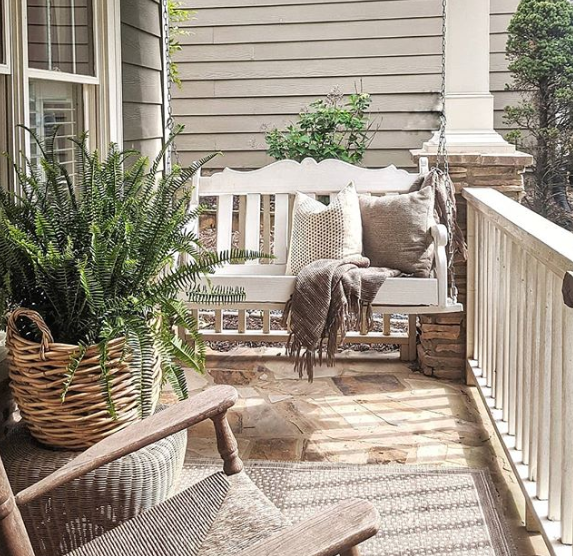 Front porch swinging bench with throws and pillows, a rocking chair, and plants. 